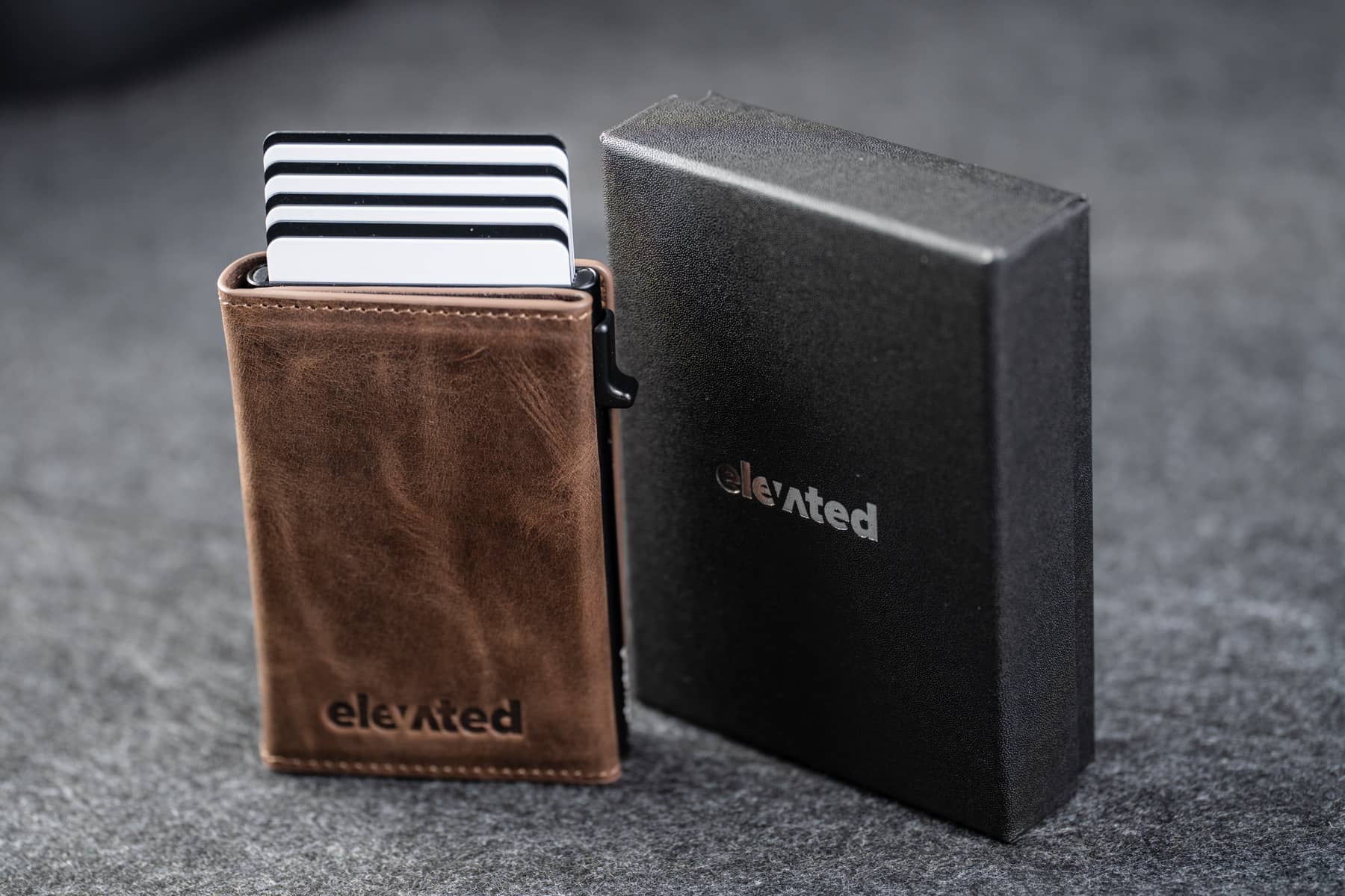 Šokolaadipruun kaarditasku Elevated Slim 2.1 (KT012) pop-up mehhanismiga, mis toob kaardid mugavalt välja. Kõrval elegantne must kinkekarp.